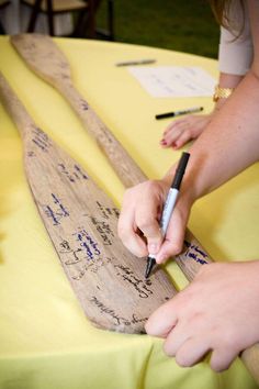 a person writing on a piece of wood at a table with other people around it