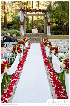 an outdoor ceremony with red and white flowers on the aisle