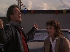 a man and woman standing next to each other in front of a car with flags on the roof