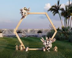 a wedding arch with flowers and candles on the grass in front of some palm trees