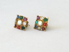 A Pair of 22ct gold earstuds with nine precious and semi-precious stones (Navratan) from North India The stones are Zirkon, Pearl, Coral, Hessonit, Saphire, Emerald, Cats Eye and Turquoise 1,2cm x 1,2cm 5,0 grams Ruby is the gem for the Sun, natural pearl for the Moon, red coral for Mars, emerald for Mercury, turquoise for Jupiter, diamond for Venus, blue sapphire for Saturn, hessonite for Rahu (ascending lunar node), and cat's eye for Ketu (descending lunar node). A very powerful protection and Temple Jewelry Earrings With Stones As Gift, Temple Jewelry Earrings With Stones For Gift, Festive Yellow Gold Multi-stone Earrings, Navratan Earrings, Indian Jewelry Earrings, North India, Cats Eye, Gold Earrings Designs, Natural Pearl