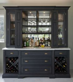 a black cabinet with wine glasses and bottles on the top is in front of a window