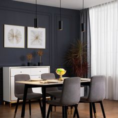 a dining room table with grey chairs and artwork on the wall in front of it