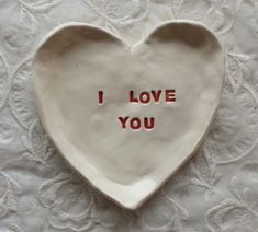 a ceramic heart shaped dish with the words i love you written in red on it