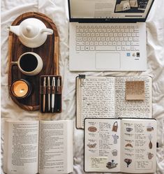 an open laptop computer sitting on top of a white bed next to two notebooks