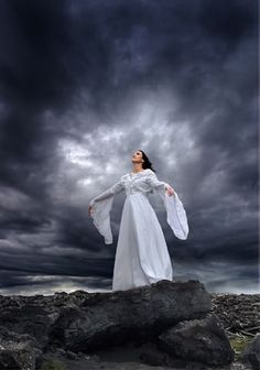 a woman standing on top of a rock under a cloudy sky