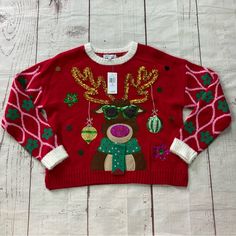 a red sweater with reindeer and christmas decorations on the front is sitting on a white wooden floor