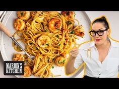 a woman holding up a plate of pasta with shrimp on it