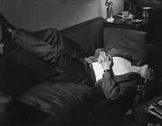 a man laying on top of a couch next to a table with a book in his hand