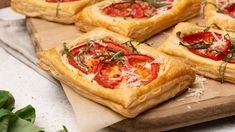 several small pizzas with tomatoes and cheese on a cutting board next to some greens