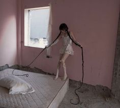 a woman in white dress standing on top of a mattress next to a window with no curtains