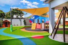 An outdoor childcare playground with a large blue and red airplane with slides in the middle of the playground with a yellow cartoon looking road around it. Around the road there is grass. It is sheltered by a yellow sail shade and has a wooden climbing board. Daycare Rooms Setup, Daycare Rooms, Toddler Playground, Preschool Program, School Interior, Home Daycare, Montessori Classroom