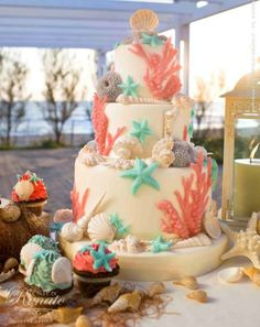 a wedding cake with seashells and starfish on the top is surrounded by shells