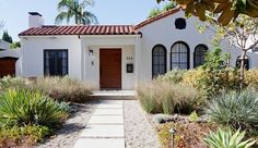 a white house with lots of plants in front of it and a walkway leading to the door