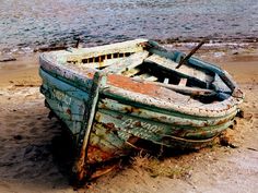 an old boat sitting on top of a sandy beach