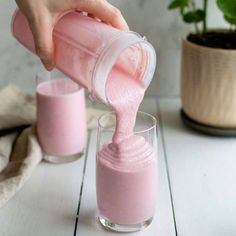 a person pouring pink liquid into a glass on top of a white table next to a potted plant