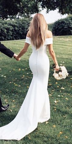 a bride and groom hold hands as they walk through the grass