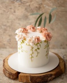 a white cake with pink flowers on top sitting on a wooden stand next to a marble wall