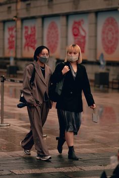 two people walking down the street wearing masks