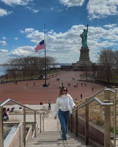 a woman is walking up some stairs in front of the statue of liberty