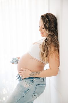 a pregnant woman leaning against a wall with her stomach exposed and tattoos on her belly