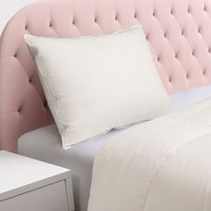 a pink headboard with two pillows and a night stand in front of the bed