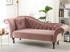 a pink couch sitting on top of a white rug next to a table with a potted plant