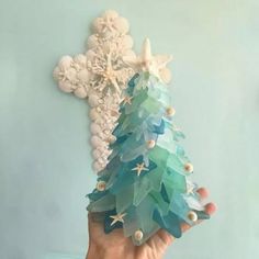 a hand holding a small christmas tree made out of sea glass and seashells