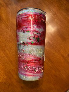 a red and white vase sitting on top of a wooden table next to a candle