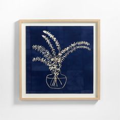 a blue and white framed artwork with plants in a vase on the wall next to it