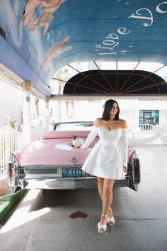 a woman standing in front of a pink car