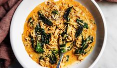 a white bowl filled with pasta and spinach on top of a table next to a napkin