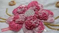 a pink and white flower is sitting on a table cloth next to some gold thread