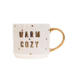 a white and gold coffee mug with the words warm cozy printed on it's side