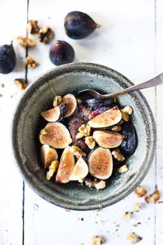 a bowl filled with figs and nuts on top of a white wooden table next to a spoon