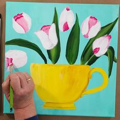 a painting of flowers in a yellow cup on a blue background, with a person's hand holding a pencil