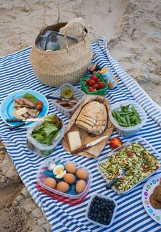 a blue and white striped towel with food on it, including bread, salads, eggs, fruit, and vegetables