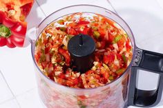 a food processor filled with chopped vegetables on top of a white tile floor next to a red pepper