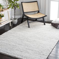 a chair sitting on top of a wooden floor next to a white rug and potted plant