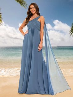 a woman standing on the beach wearing a blue dress with one shoulder draped over it