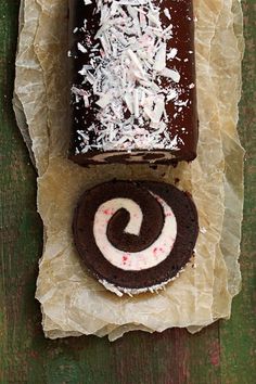 a piece of chocolate cake next to a roll on wax paper with coconut sprinkles