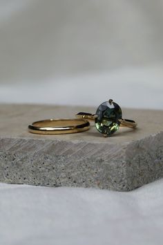 two gold rings sitting on top of each other next to a stone block with a green ring