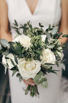 a bridal holding a bouquet of white roses and greenery