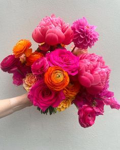 a bouquet of flowers is being held by someone's hand against a white wall