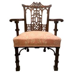 an ornately carved wooden chair with pink upholstered seat and back cushion, on white background