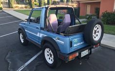 a blue suzuki truck parked in a parking lot next to a house with two doors open