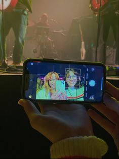 a person holding up a cell phone to take a selfie with the band on stage in the background