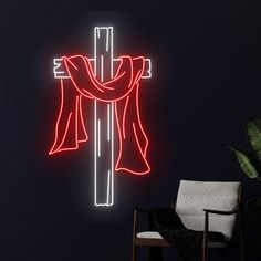 a neon cross is lit up against a dark wall with a chair in the foreground