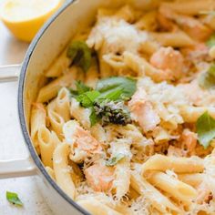 pasta with salmon and parmesan cheese in a pan next to lemon wedges