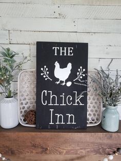 a sign that says the chicken inn on it next to some potted plants and pine cones